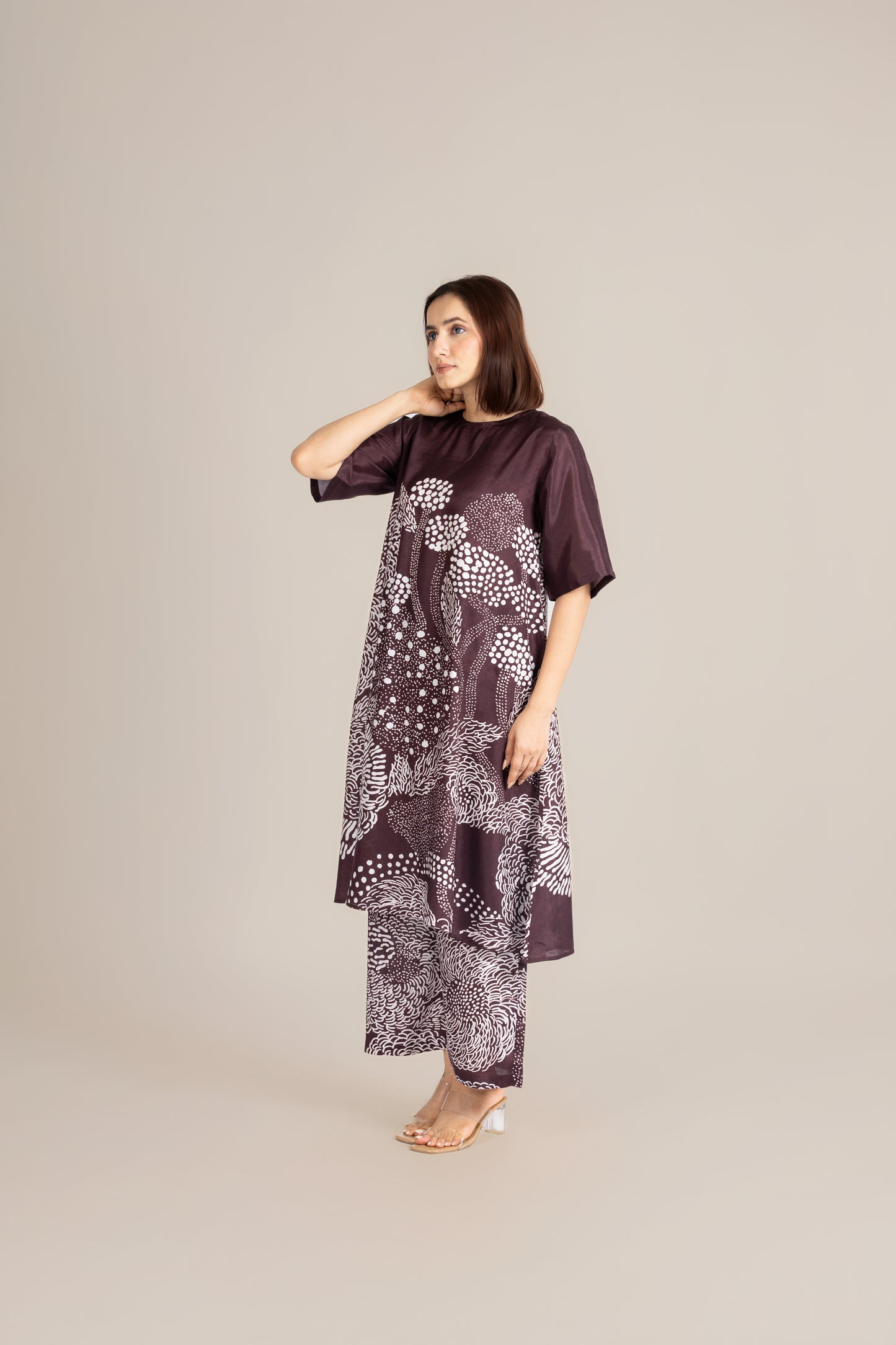 Woman wearing a dark brown dress with white floral patterns on a beige background