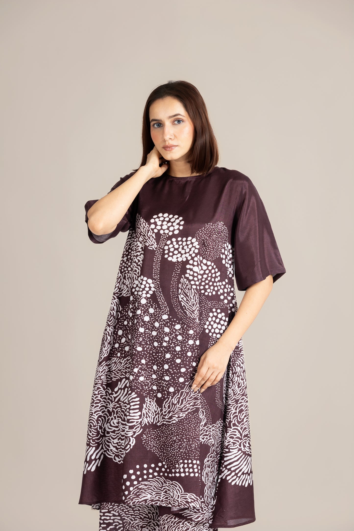 Woman wearing a dark brown dress with white floral pattern on a plain background