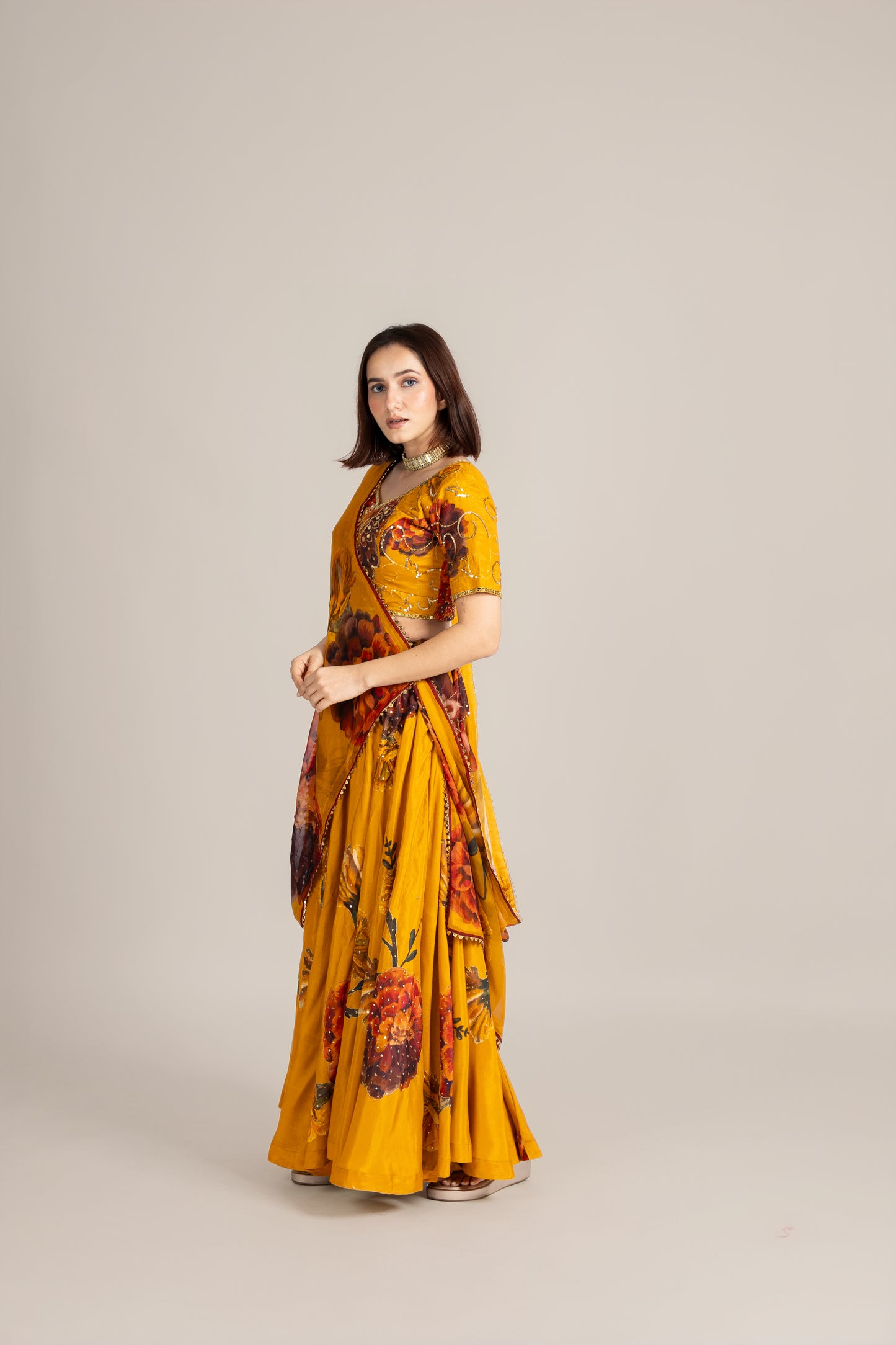 Woman wearing a yellow saree with floral patterns on a beige background