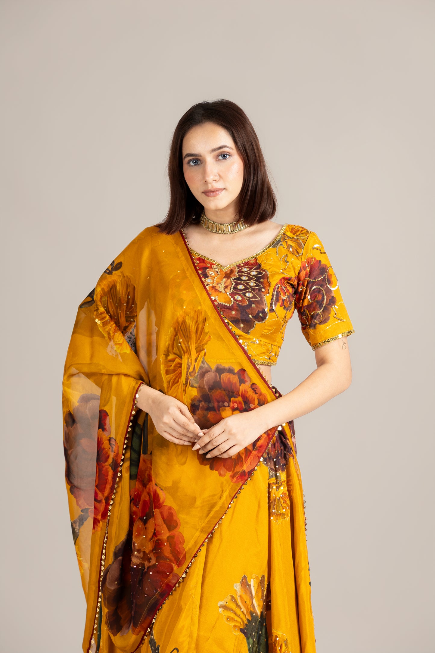Woman wearing a yellow saree with floral patterns on a plain background