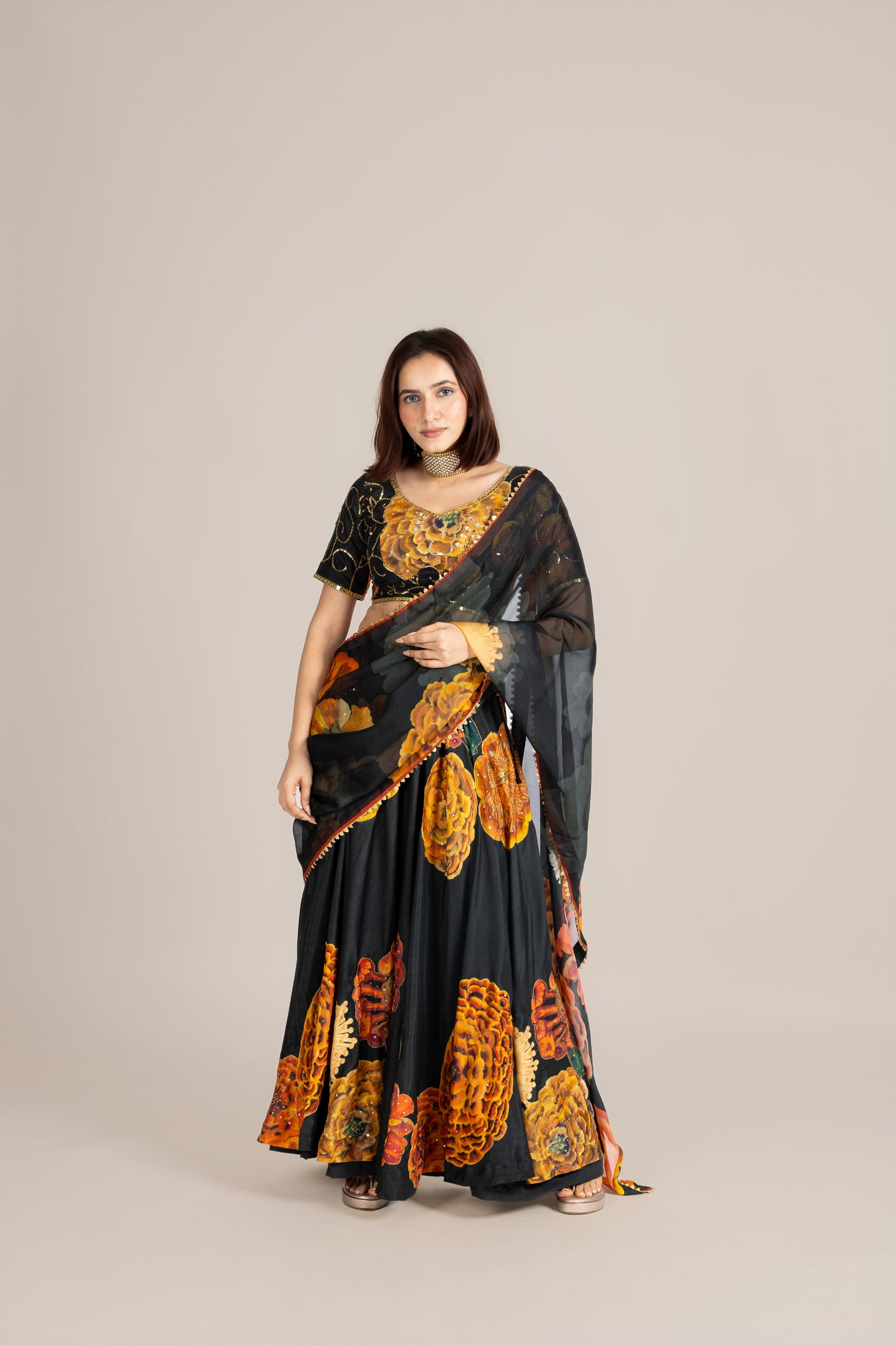 Woman wearing a black and orange floral saree on a beige background