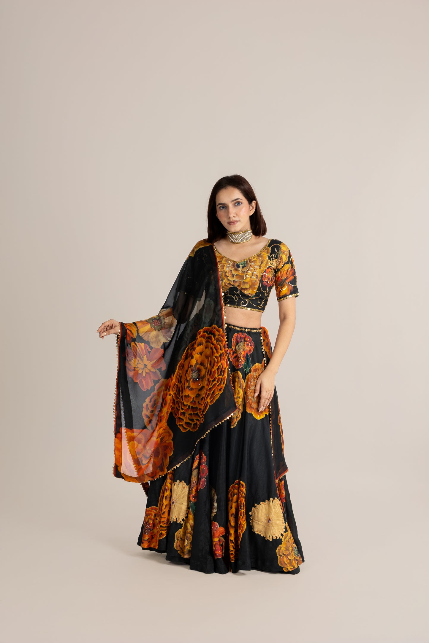 Woman wearing a black and orange patterned outfit with a matching dupatta on a beige background