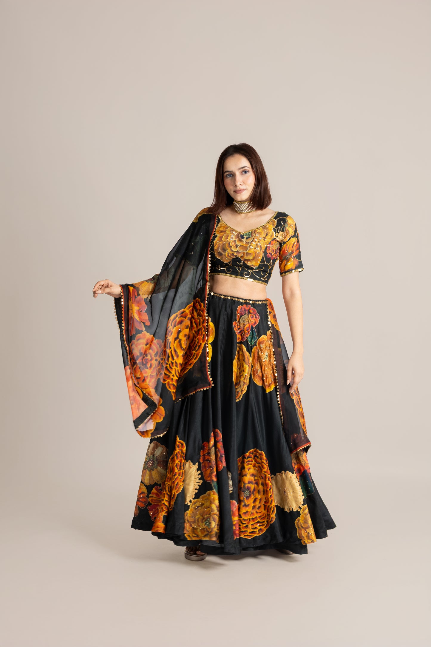 Woman wearing a black and orange traditional outfit with a matching dupatta on a beige background